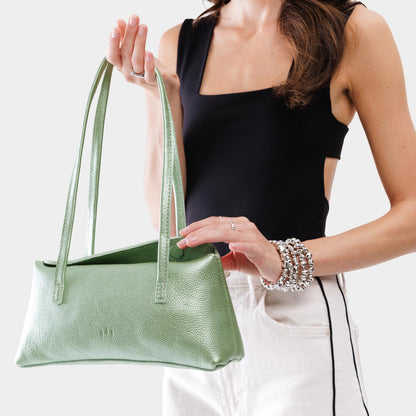 Beetle | Woman holding a shiny green leather bowler bag against a white background