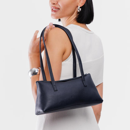 Night Owl | Woman wearing a navy blue leather bowler bag against a white background