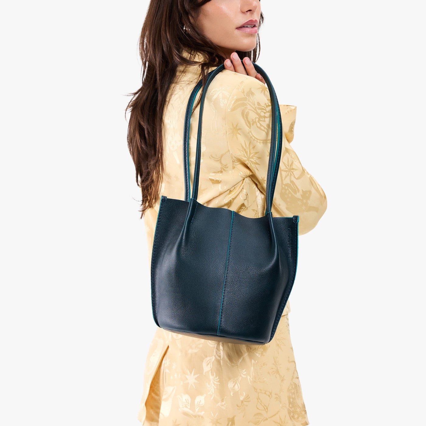 Boreal*Small | Model wearing matching light yellow shirt and trousers carrying petite bucket shaped tote bag with matching leather handles