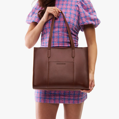 Cognac*East/West | Model holding structured wide tote bag with overlapping panels and crossbody strap