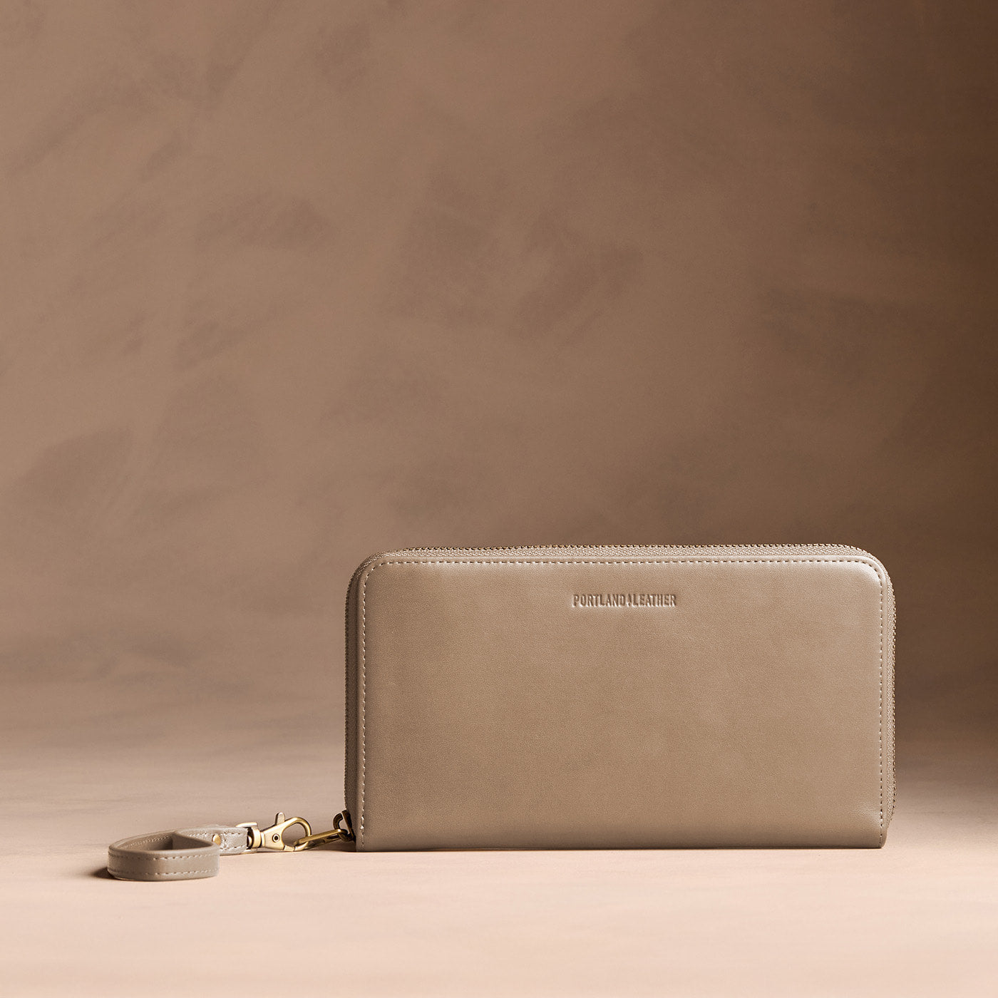 Satine | Full zip around wallet with a strap on a brown background