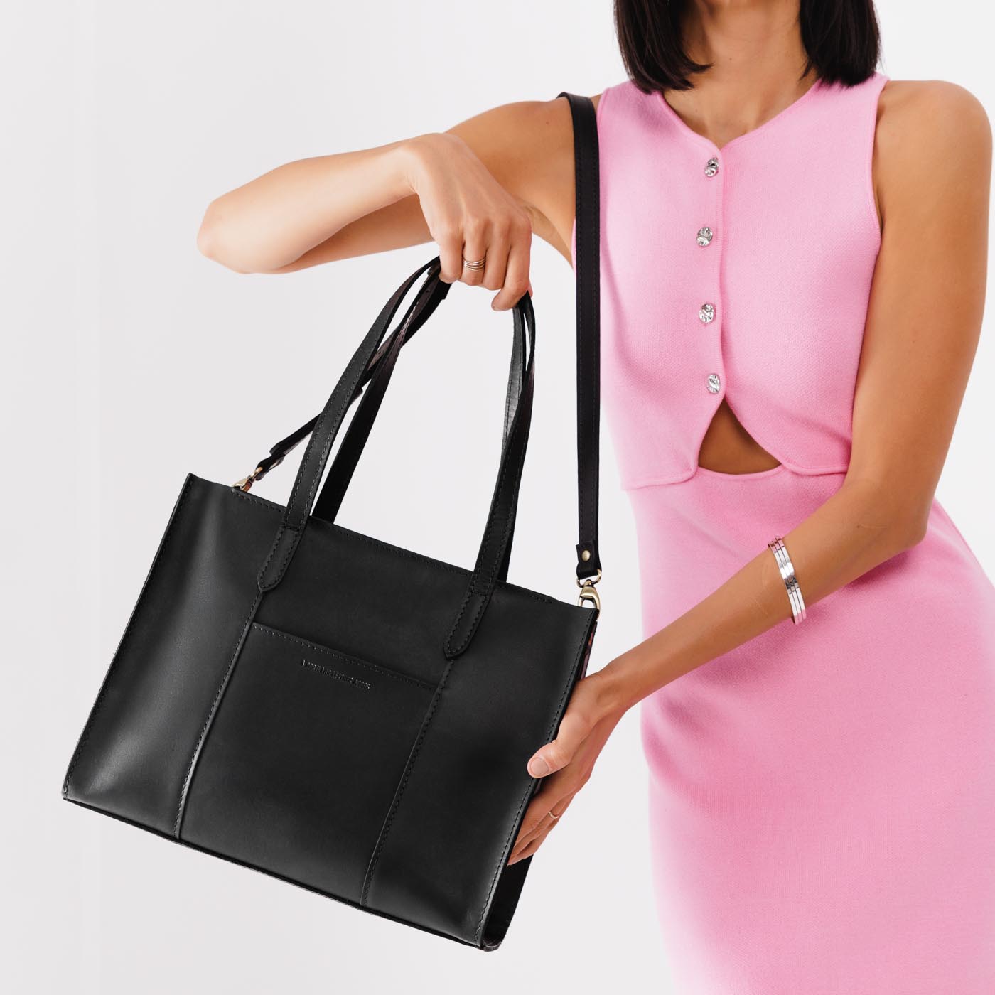 Black*East/West | Model holding structured wide tote bag with overlapping panels and crossbody strap