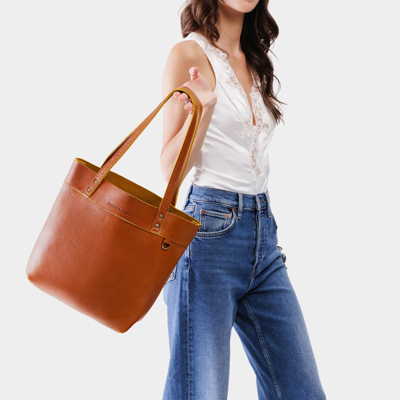 Sienna*Medium*Classic | Model holding a leather tote bag with riveted straps and exterior key loop