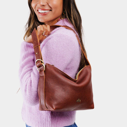 Nutmeg*Small | Model holding petite slouchy leather shoulder bag with zipper opening and three metal tree emblems
