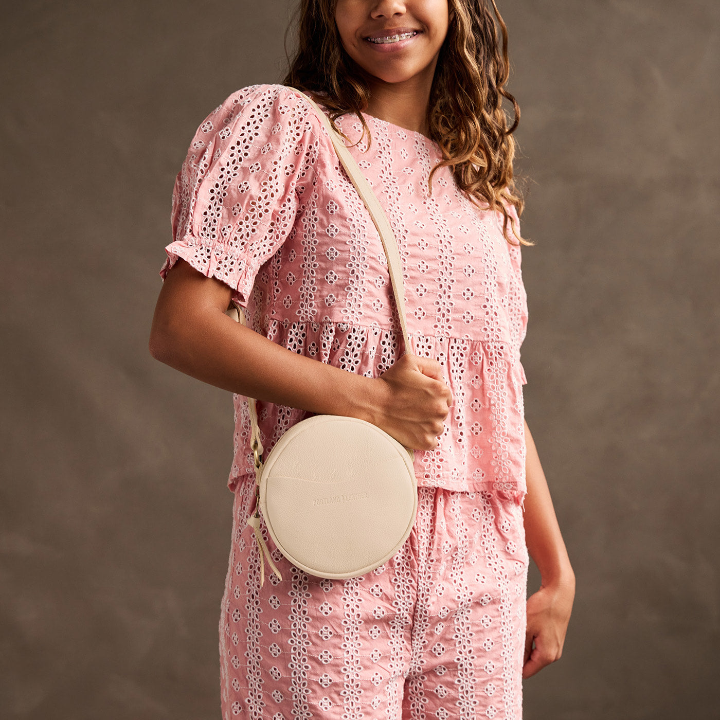 Pebbled Bone | Model wearing a circle shaped crossbody bag with top zipper and gold accents